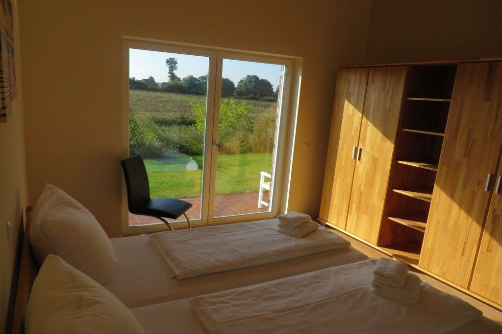 A bedroom with a bed, a chair, a wooden wardrobe, and a sliding glass door to a garden.