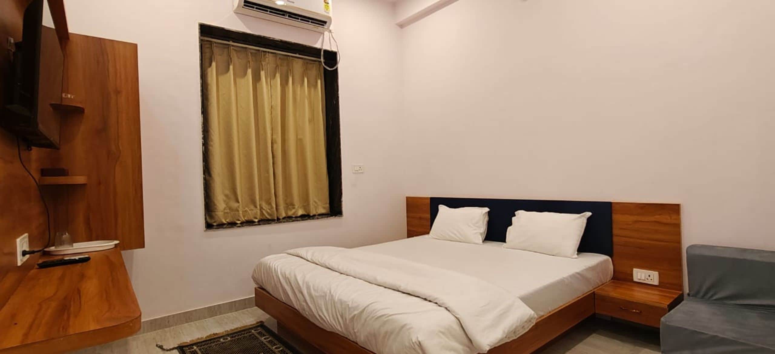 Un dormitorio con cama, mesita de noche, armario de madera, ventana con cortinas y aire acondicionado instalado en la pared.