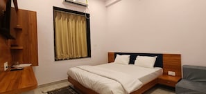 Un dormitorio con cama, mesita de noche, armario de madera, ventana con cortinas y aire acondicionado instalado en la pared.