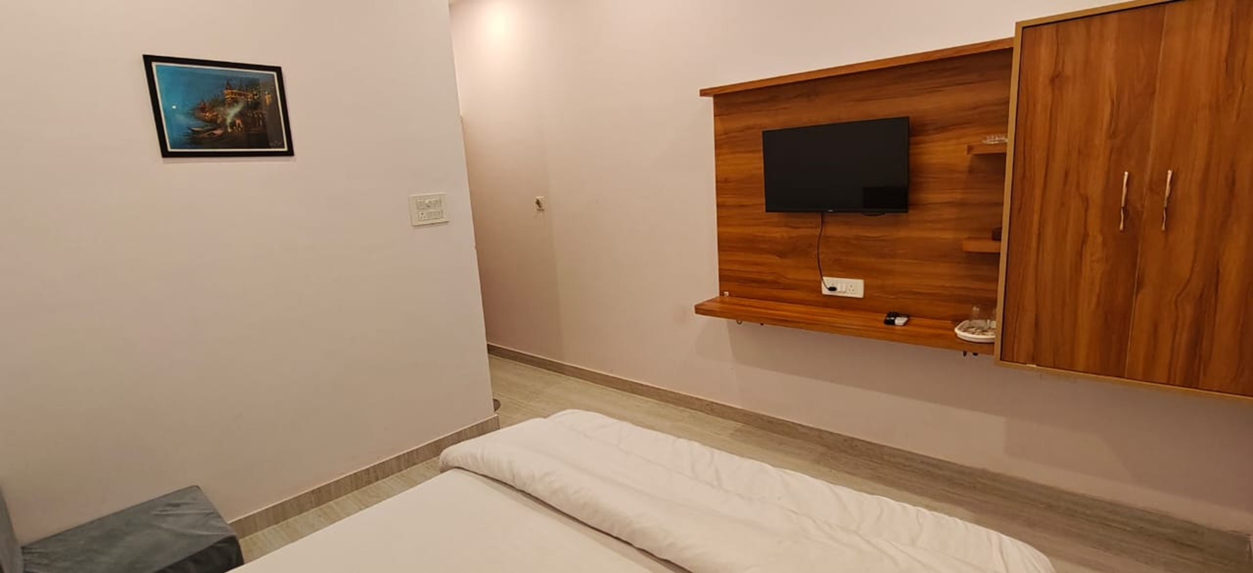 A bedroom with a bed, a mounted TV, and a wooden wardrobe.