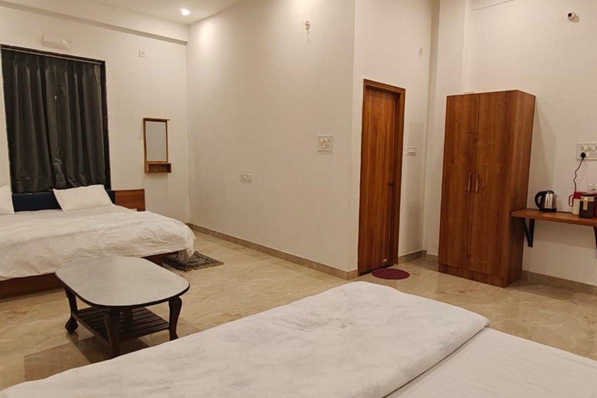 Habitación de hotel con dos camas, una mesita, un espejo, un armario y una estantería con una tetera.