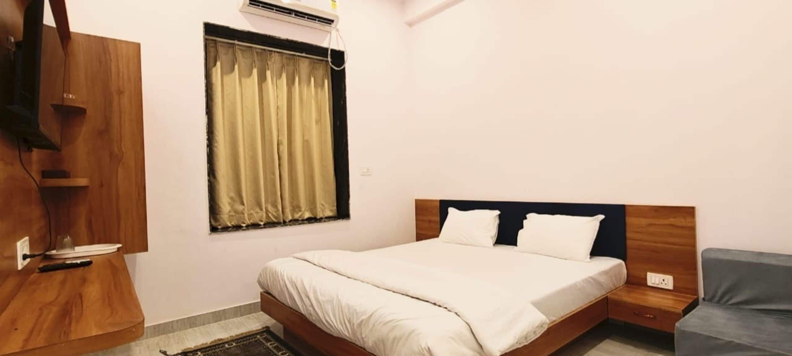 Un dormitorio con cama, mesita de noche, armario de madera, ventana con cortinas y aire acondicionado.