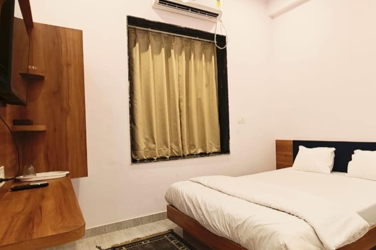 Un dormitorio con cama, mesita de noche, armario de madera, ventana con cortinas y aire acondicionado.