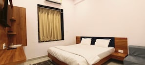 Un dormitorio con cama, mesita de noche, armario de madera, ventana con cortinas y aire acondicionado.
