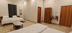 Habitación de hotel con dos camas, una mesita, un espejo, un armario y una estantería con una tetera.