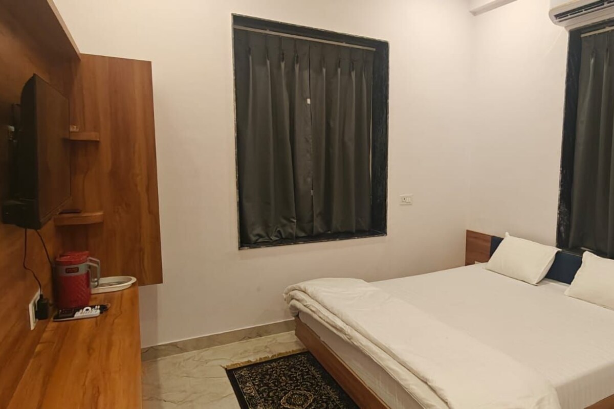 Un dormitorio con cama, armario de madera, televisor y dos ventanas con cortinas.