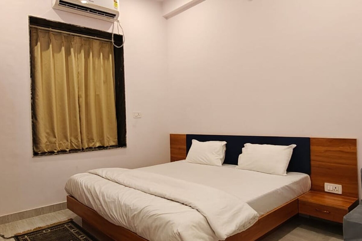 Un dormitorio con cama, mesita de noche, armario de madera, ventana con cortinas y aire acondicionado instalado en la pared.