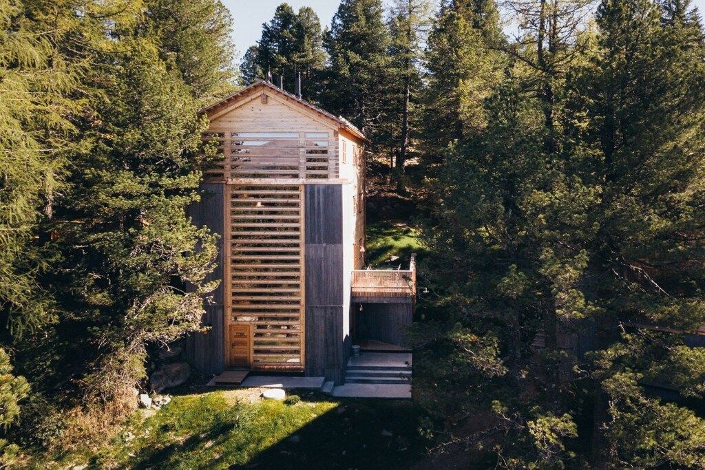 A wooden cabin with a sloped roof, surrounded by dense forest.
