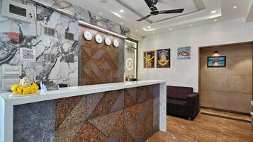 Zona de recepción de un hotel con una pared de mármol, un mostrador de recepción y un ventilador de techo.