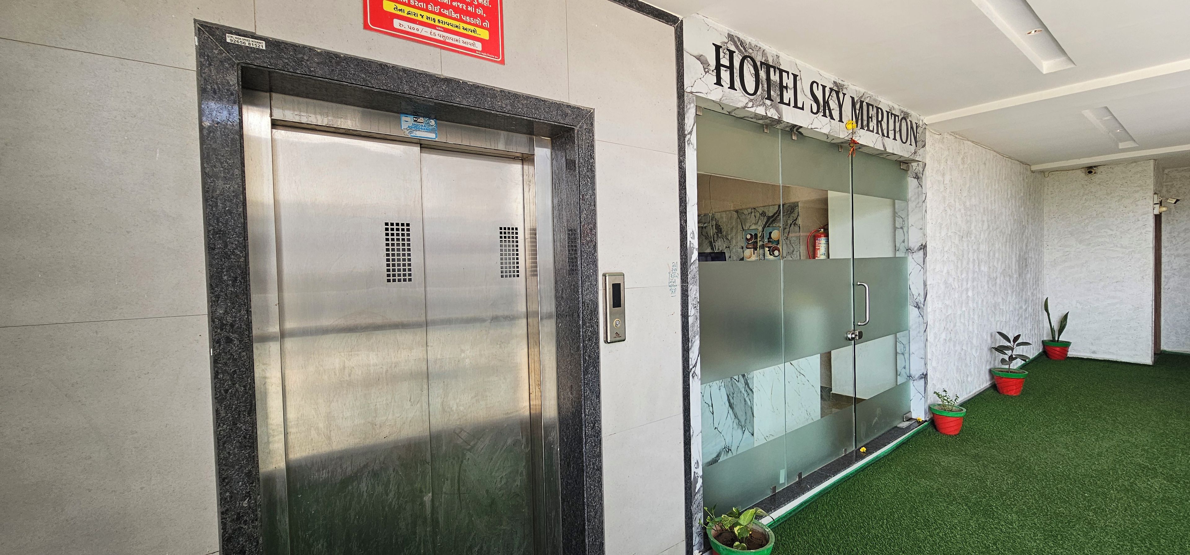 An elevator with a sign above it, a reception area with a glass partition, and a sign for 'HOTEL SKY MERITON'.