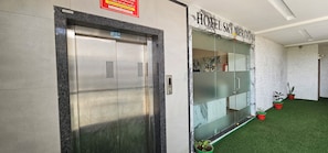 Un ascensor con un cartel encima, un área de recepción con un panel de vidrio y un cartel que dice 'HOTEL SKY MERITON'.