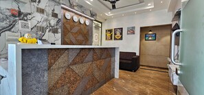Zona de recepción de hotel con un mostrador de mármol, área de descanso y una pared con relojes y obras de arte enmarcadas.