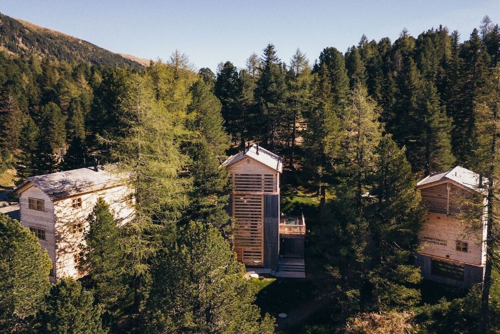 A forested area with several cabins, each with a distinct architectural style, surrounded by dense trees.