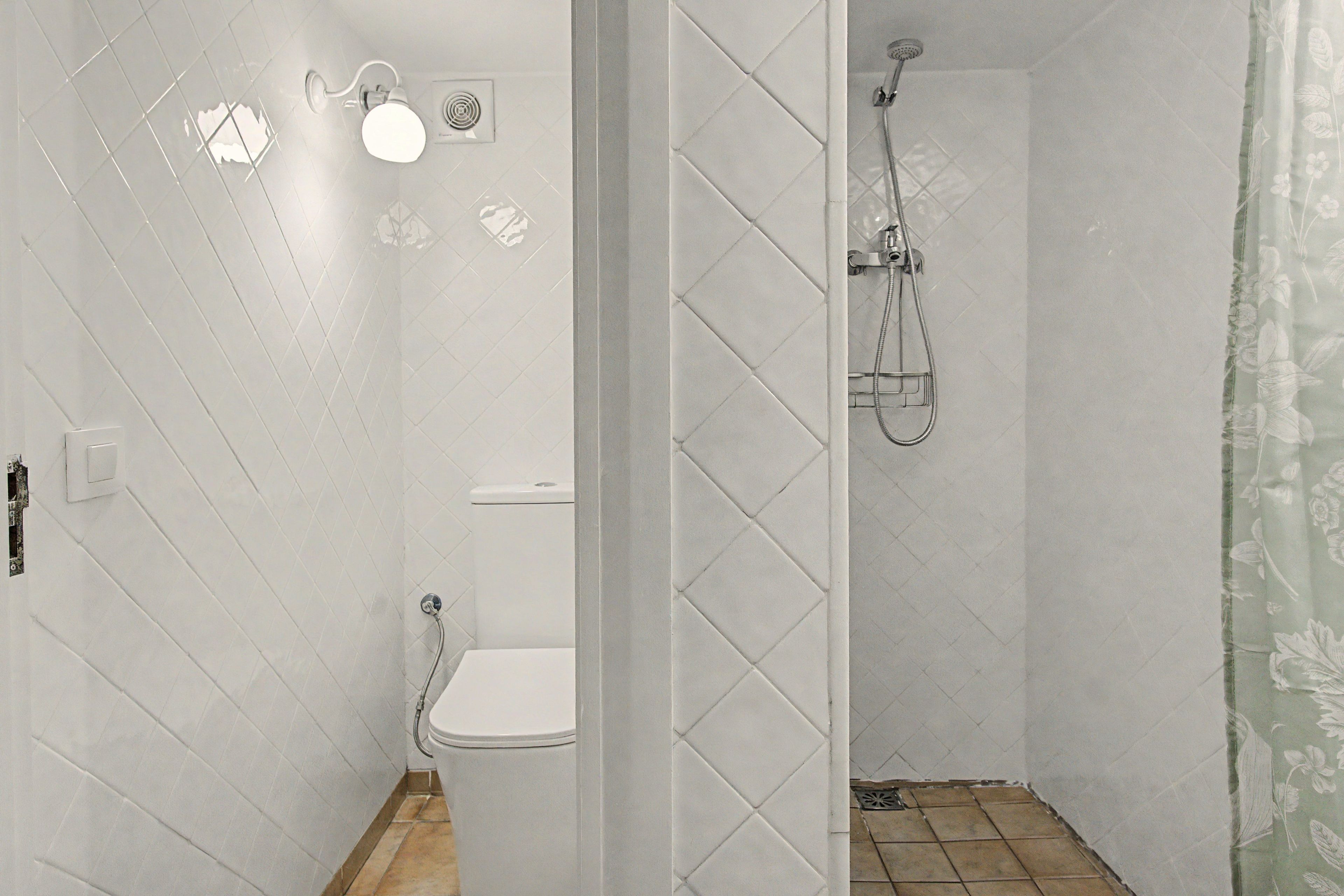 A bathroom with a toilet, a shower with a hose, and a wall-mounted light fixture.