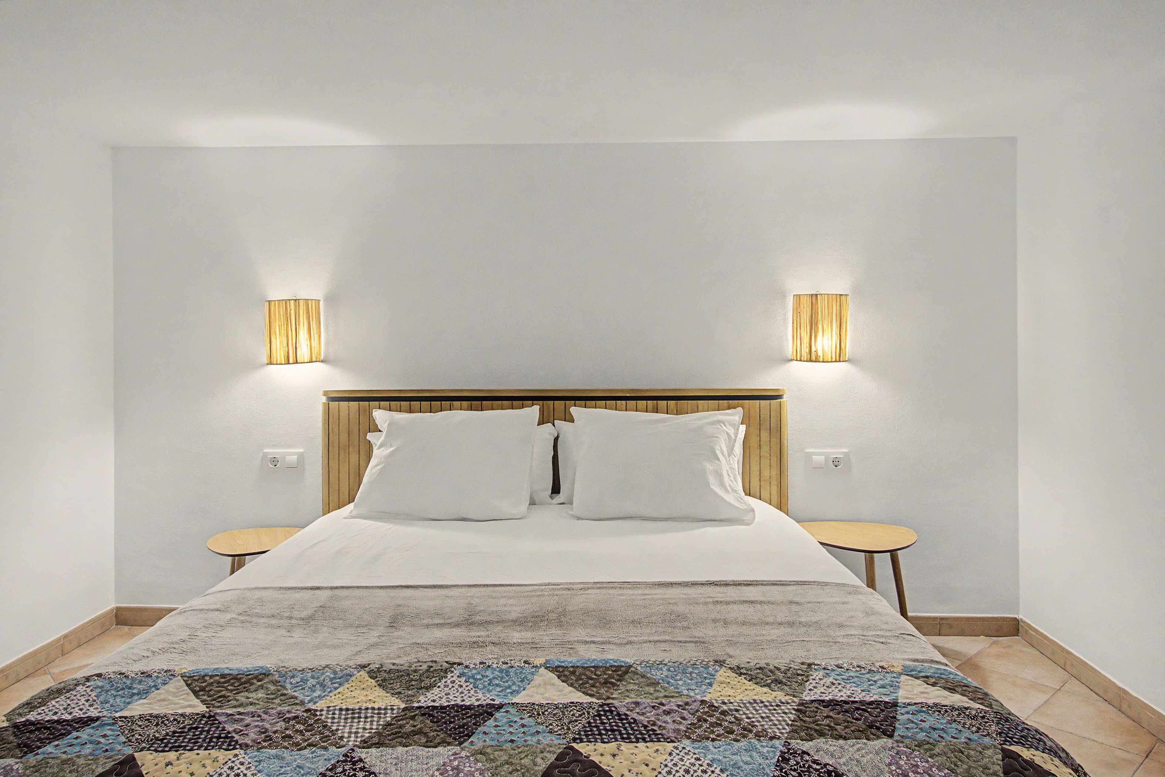 A hotel room with a bed, two bedside tables, a wooden headboard, and two wall-mounted lamps.