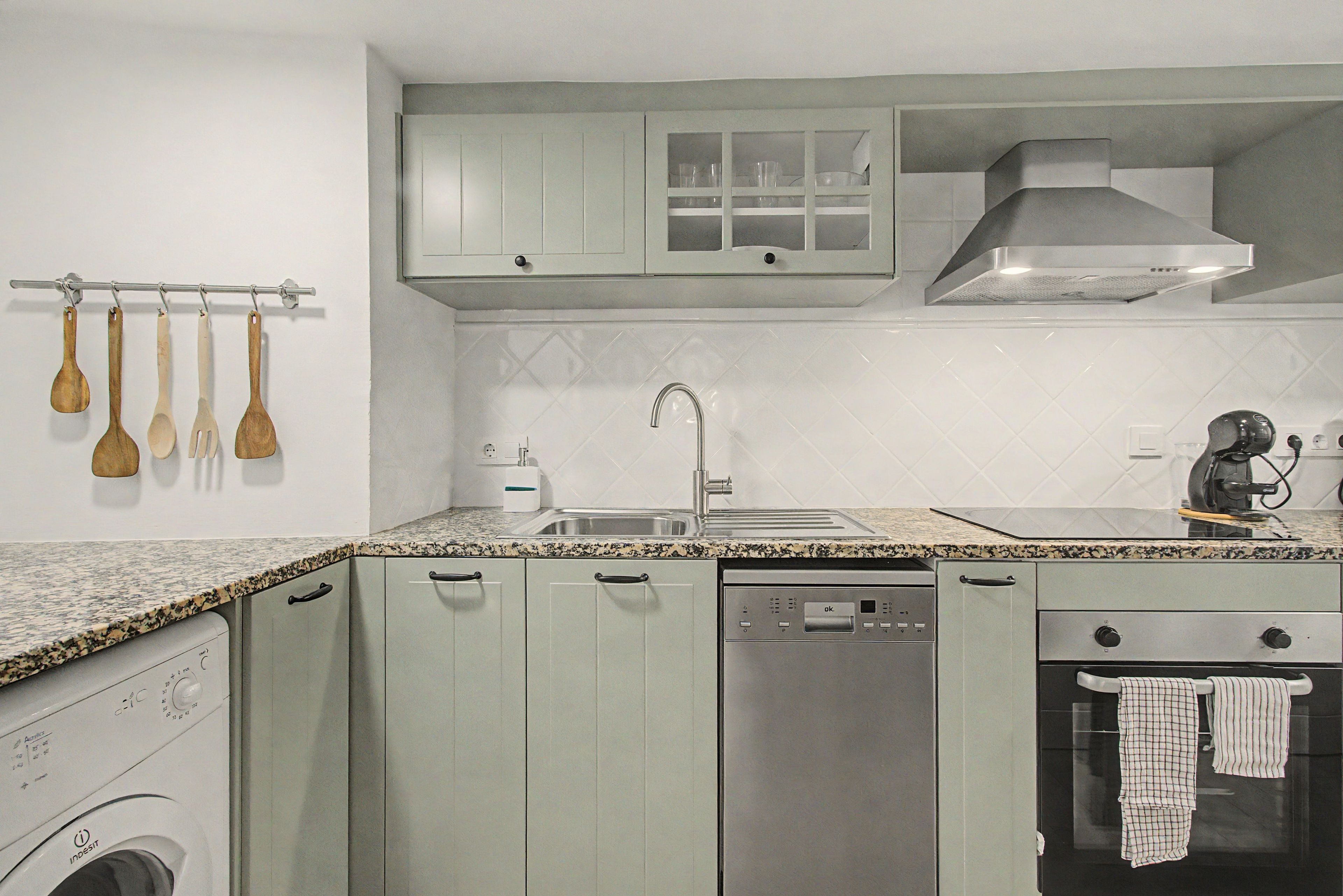 A kitchen with a washing machine, dishwasher, oven, and a coffee machine.
