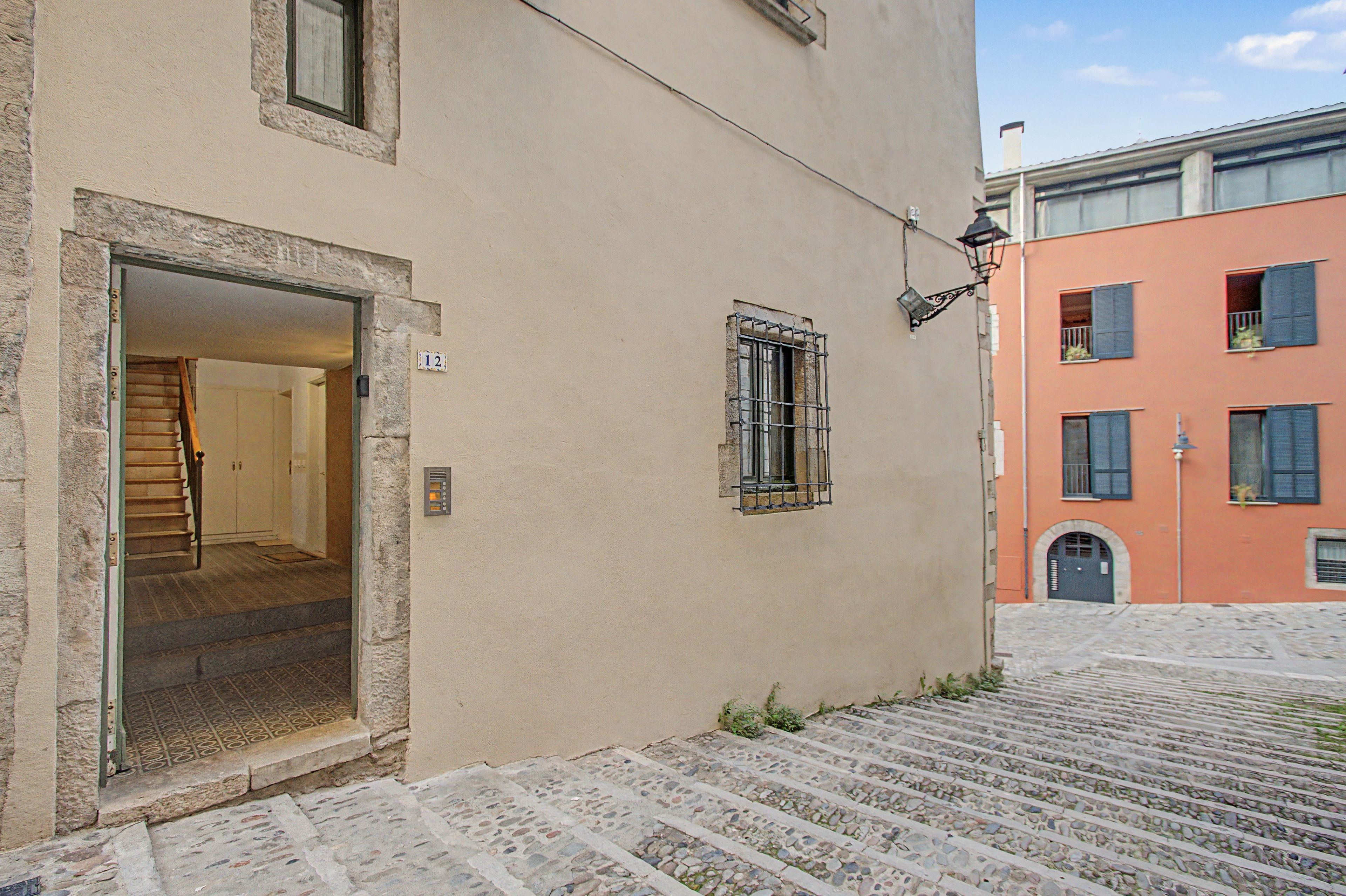 A building with a stone staircase leading to a door, a window with metal bars, and a small outdoor area with a lamp.