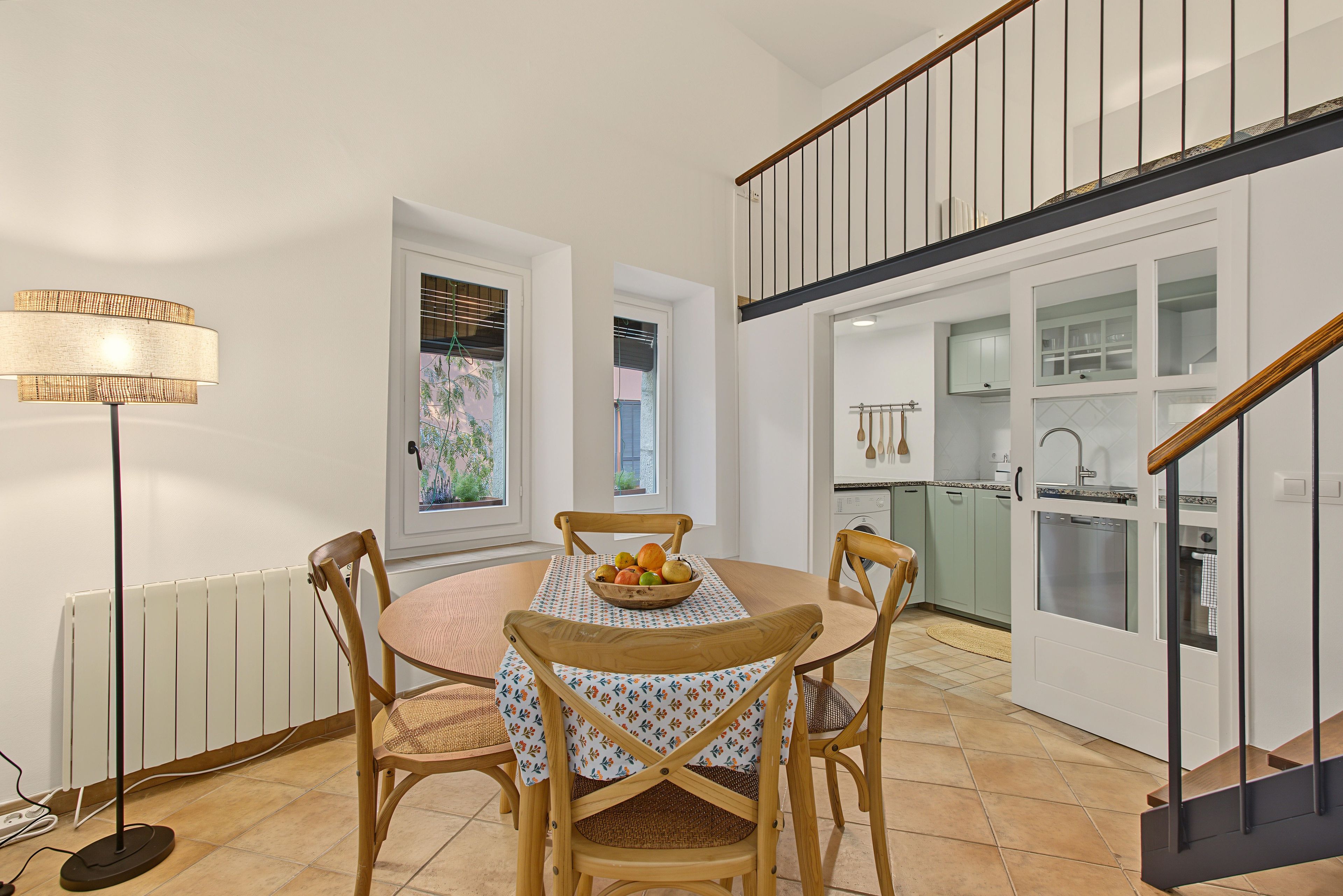 A dining area with a table set for four, a bowl of fruit, and a floor lamp.