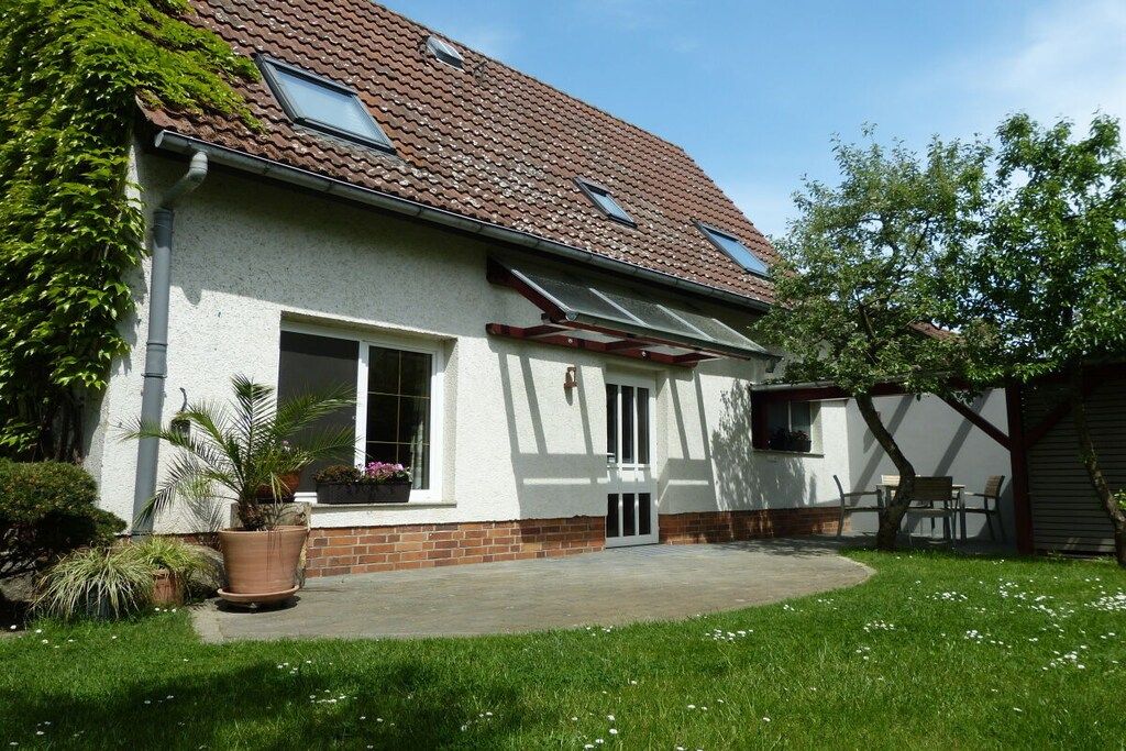 A house with a sloped roof, a covered patio, and a garden with a lawn and potted plants.