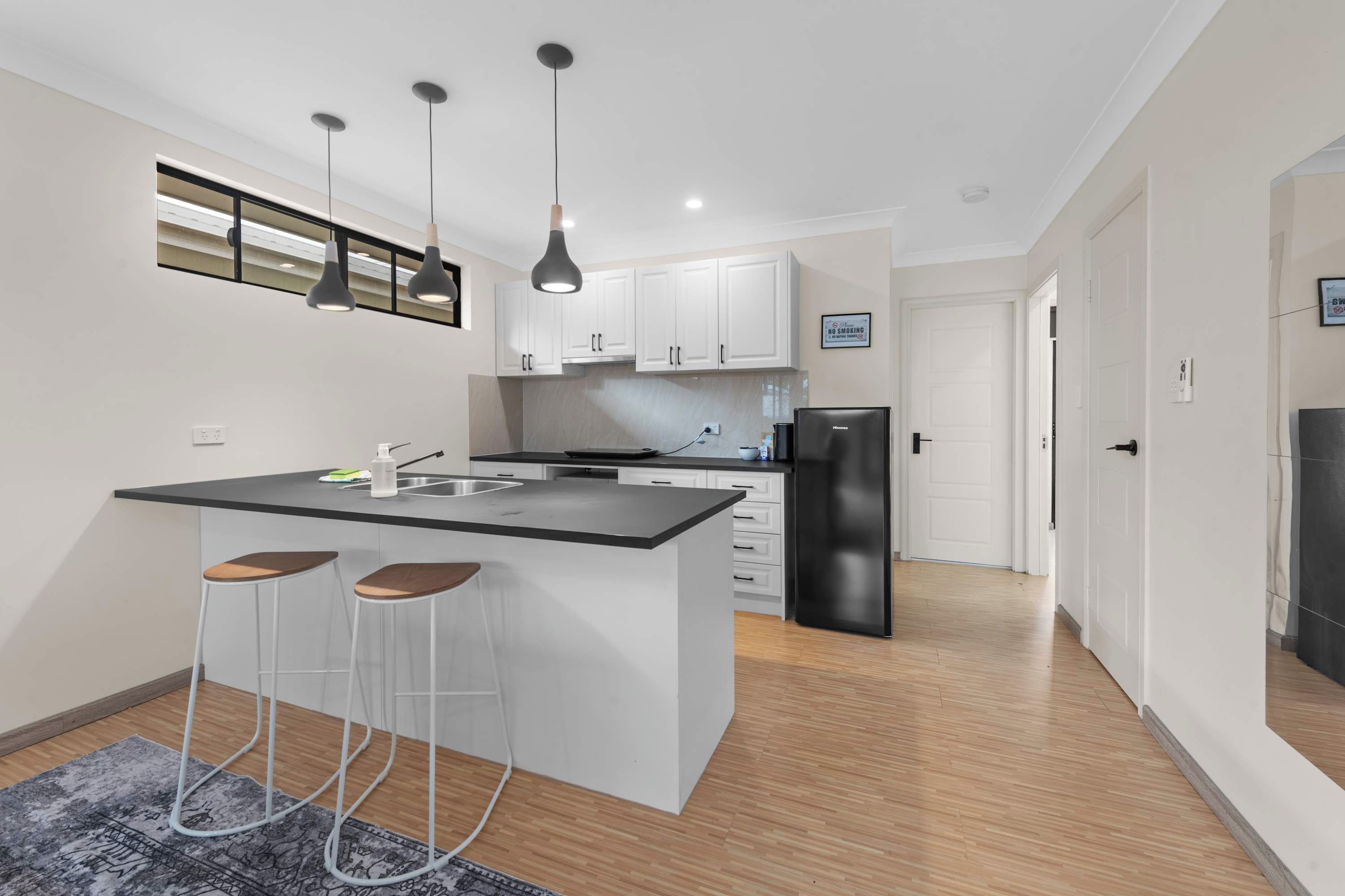 A modern kitchen with a central island, bar stools, pendant lighting, and a refrigerator.