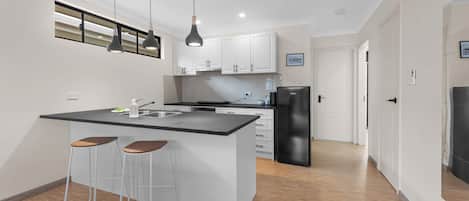 A modern kitchen with a central island, bar stools, pendant lighting, and a refrigerator.