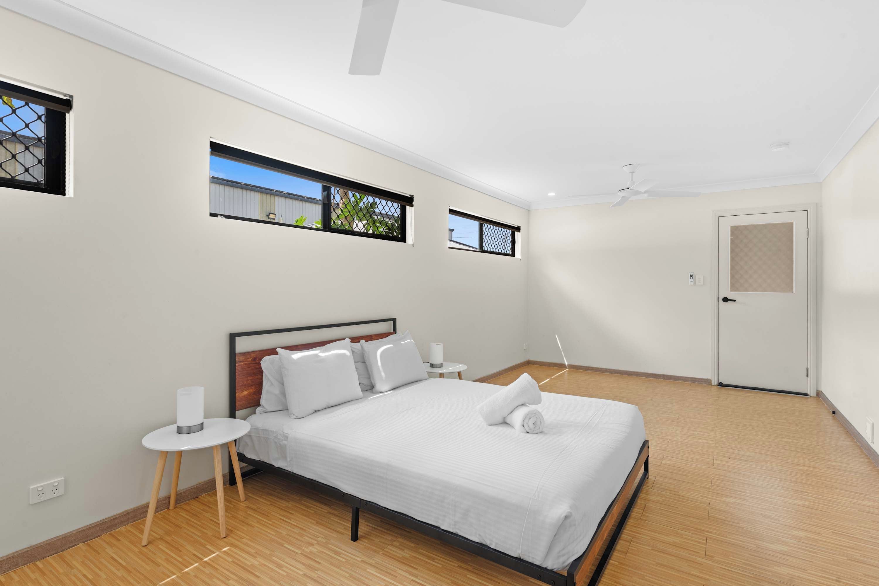 A modern bedroom with a bed, bedside tables, a ceiling fan, and windows with views.