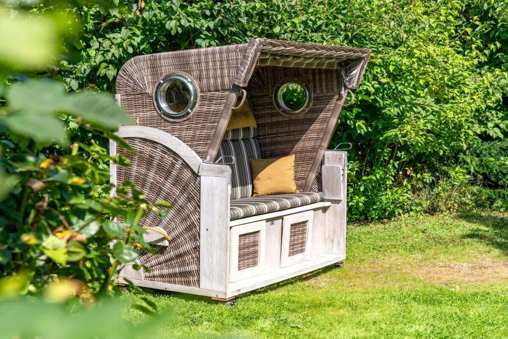 Un espacio de estar al aire libre con asientos de mimbre, un banco y una mesa pequeña, rodeado de follaje.