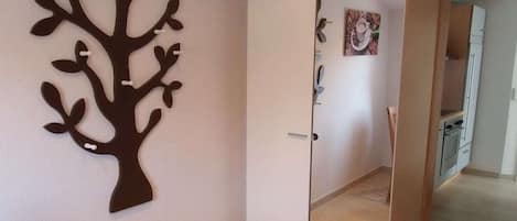 A room with a wardrobe, a wall-mounted tree decoration, and a kitchen area visible through an open door.
