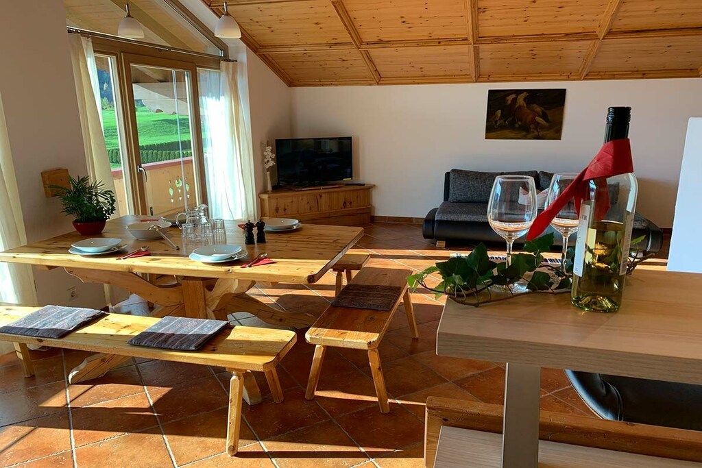 A spacious living area with a wooden ceiling, a television, a sofa, and a dining table with benches.