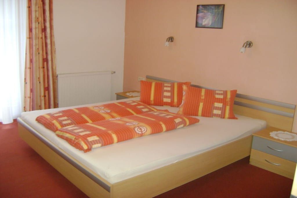Quarto com cama, mesas de cabeceira e luminária na parede.