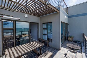 A balcony with a wooden table, a grill, and a view of the ocean. - "Serene Shores" Ocean View Luxury in Durban, South Africa (Kingsburgh)