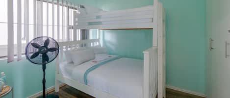 A bunk bed in a room with teal walls, a standing fan, and a window with blinds.