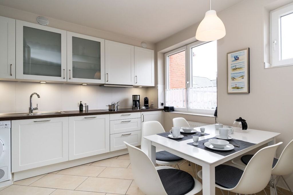 Une cuisine moderne avec des meubles blancs, une table à manger avec des chaises et une fenêtre donnant sur un beau paysage.