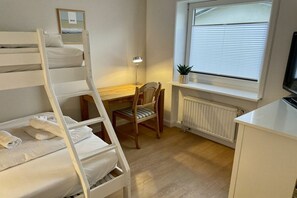 A room with bunk beds, a desk, a chair, a radiator, a window with blinds, and a television.