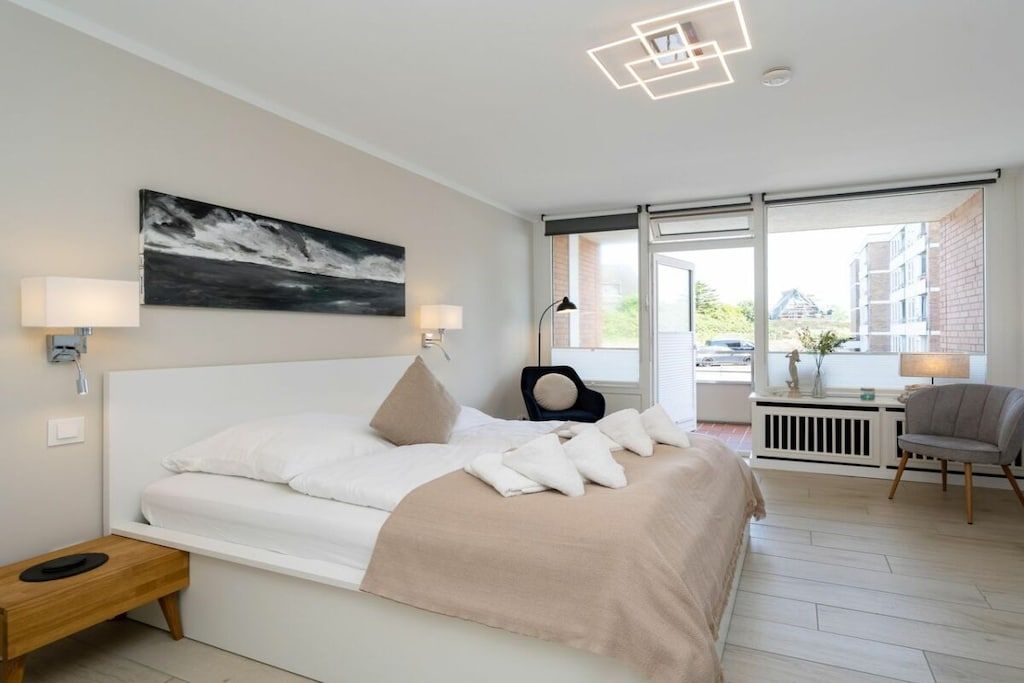 Un dormitorio moderno con cama, lámparas de noche, una ventana con vistas y una silla.