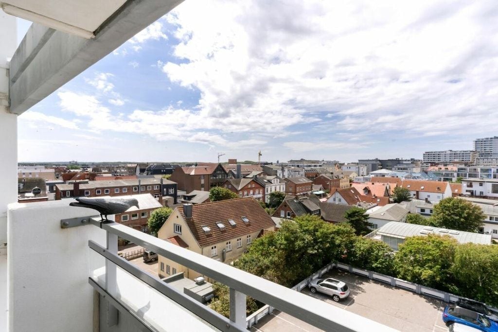 A residential area with a mix of houses and buildings, a clear sky, and a bird on a balcony railing.