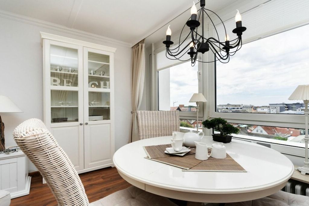 A round dining table with a white tablecloth, a chandelier, and a view of the city through large windows.