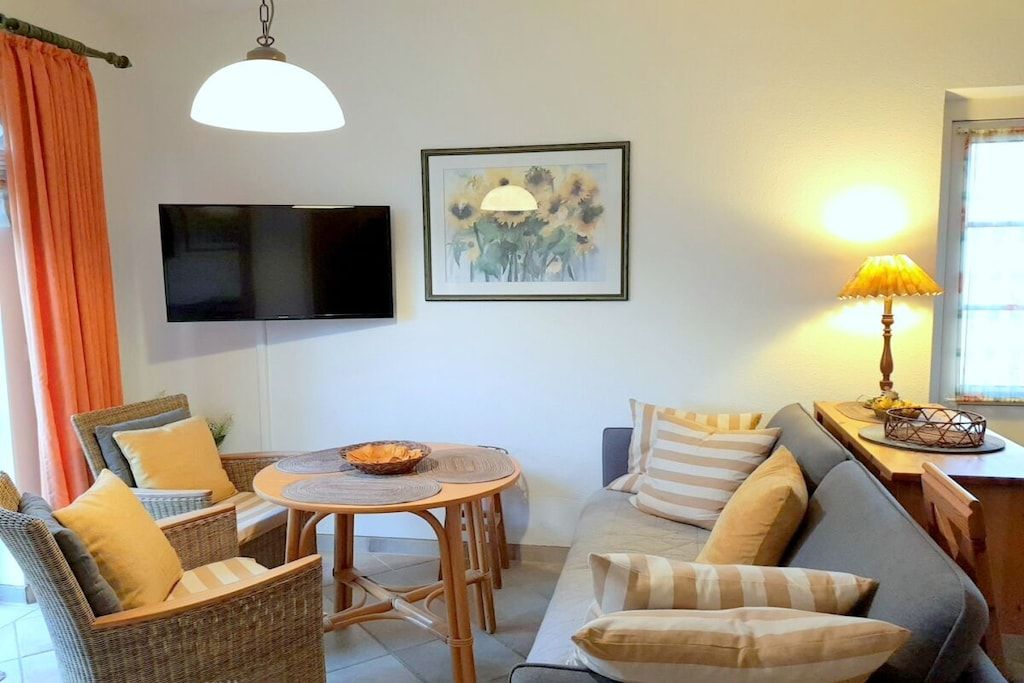 Una sala de estar con un sofá, sillas, una mesa, un televisor y una lámpara.