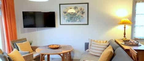 Una sala de estar con un sofá, sillas, una mesa, un televisor y una lámpara.