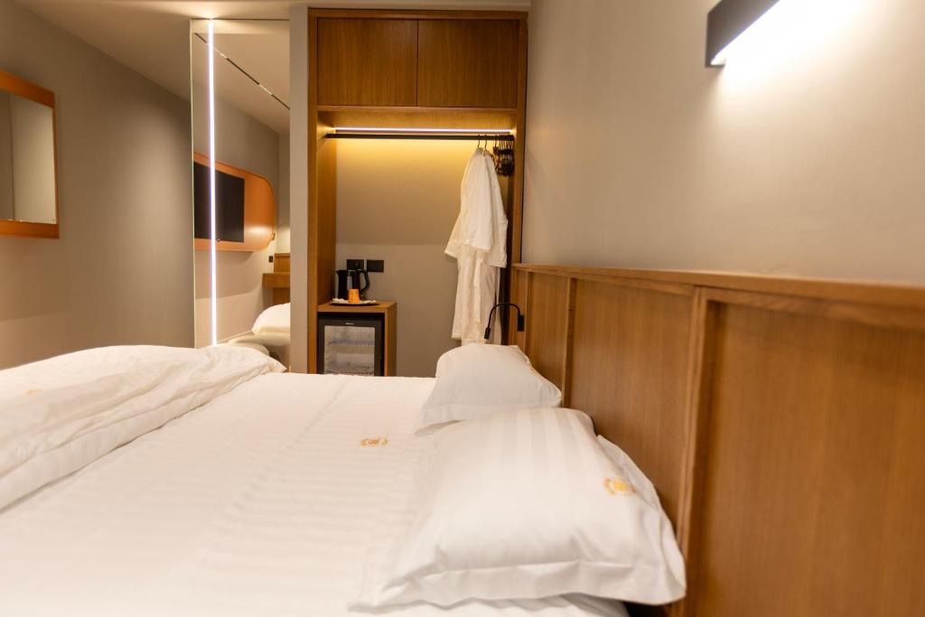 Quarto de hotel com cama, cabeceira de madeira, mesa de cabeceira com abajur e espelho.