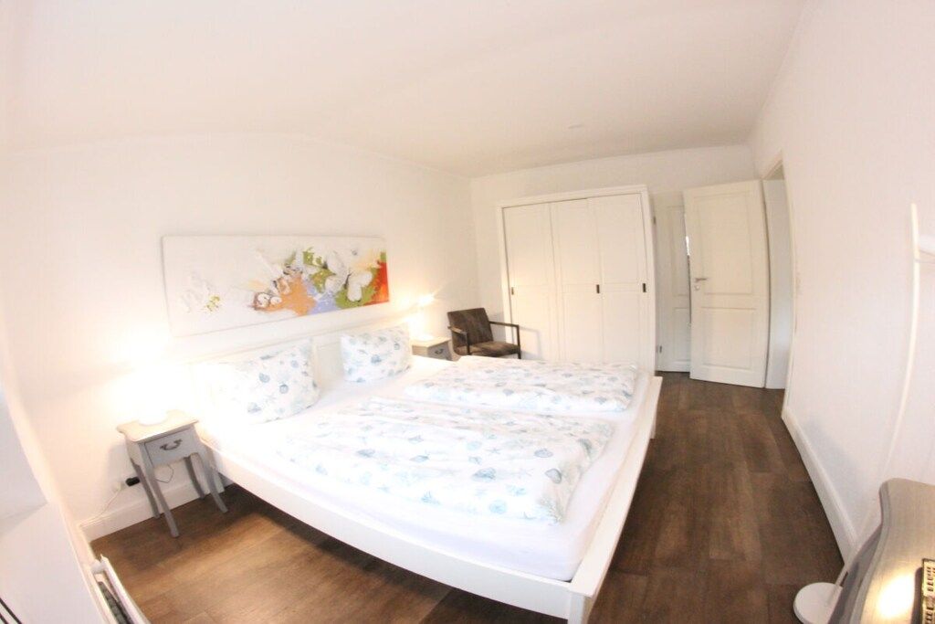 Un dormitorio con cama, mesita de noche, lámpara y un cuadro en la pared.