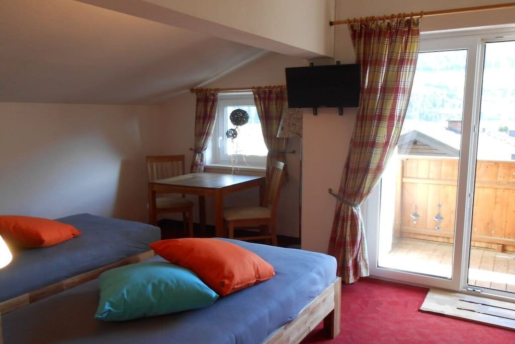 A room with two beds, a table, chairs, a TV, and a sliding glass door leading to an outdoor area.