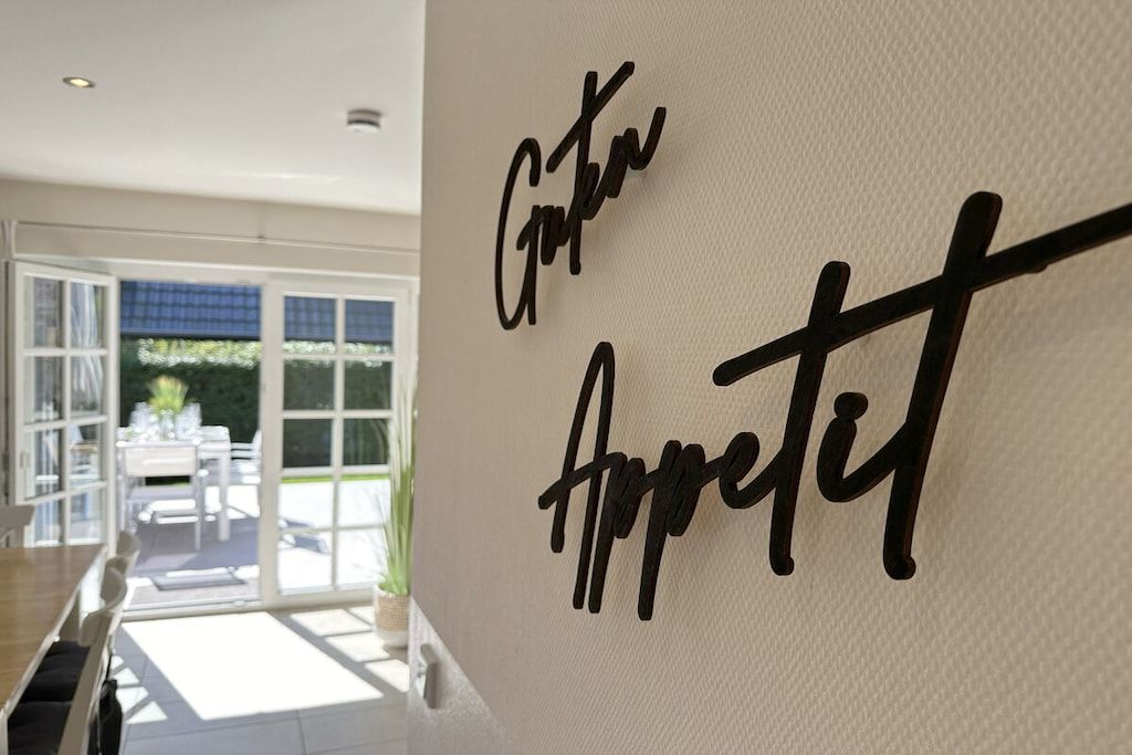 A modern interior with a wall-mounted sign reading 'Gute Appetit' and a view of an outdoor dining area.