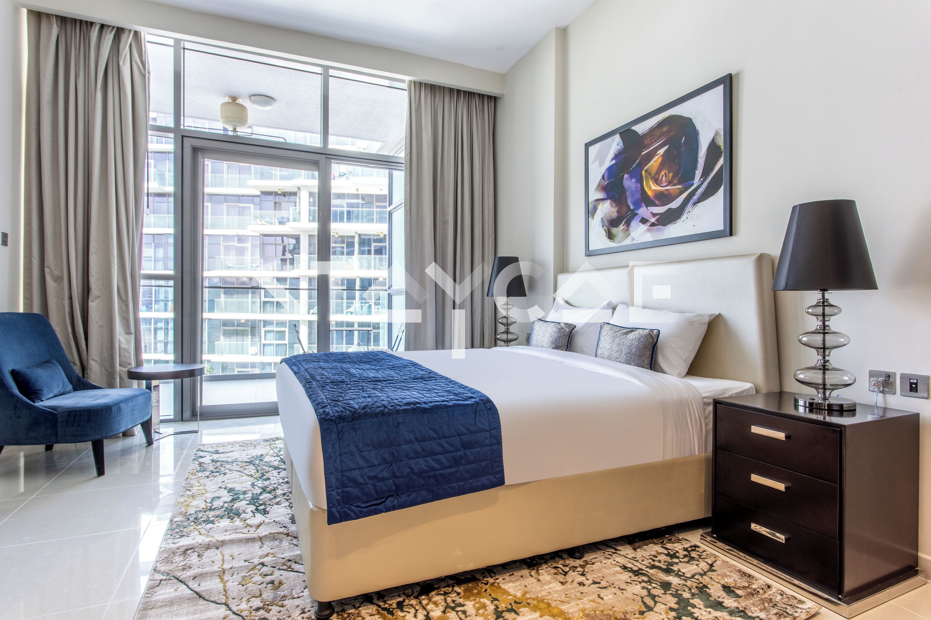 A hotel room with a large bed, a desk, a chair, a lamp, and a painting on the wall.