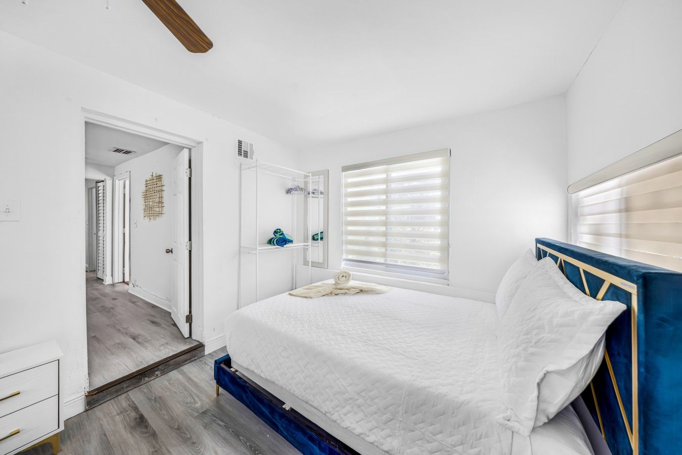 A bedroom with a bed, a wardrobe, a mirror, and a window with blinds.