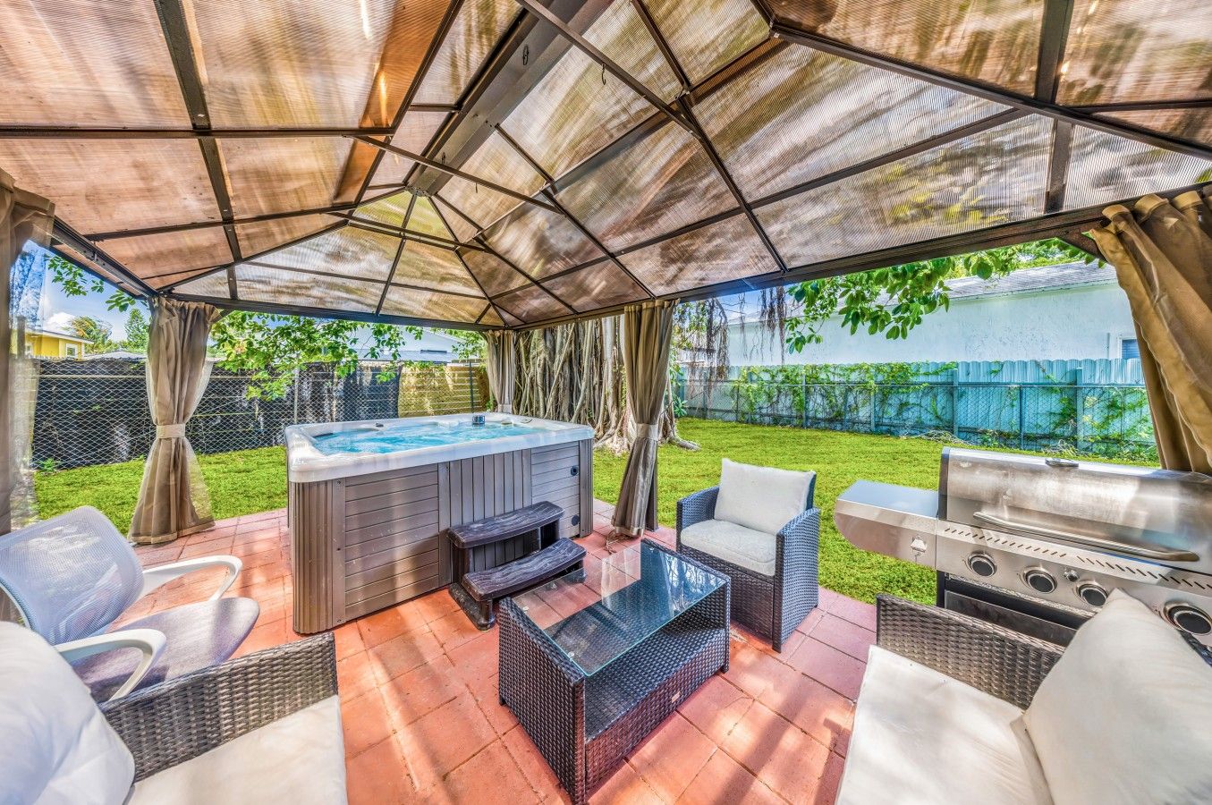 An outdoor patio with a hot tub, seating area, and a grill.
