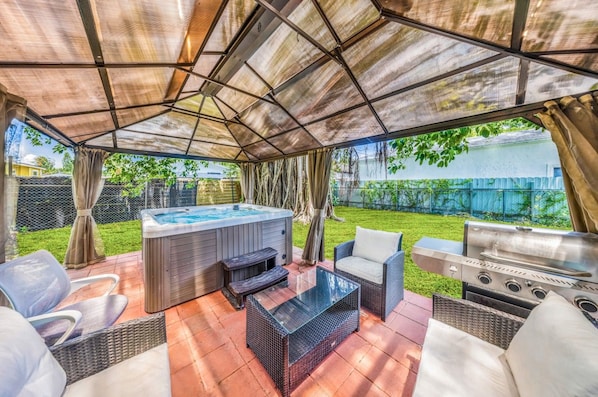 An outdoor patio with a hot tub, seating area, and a grill.