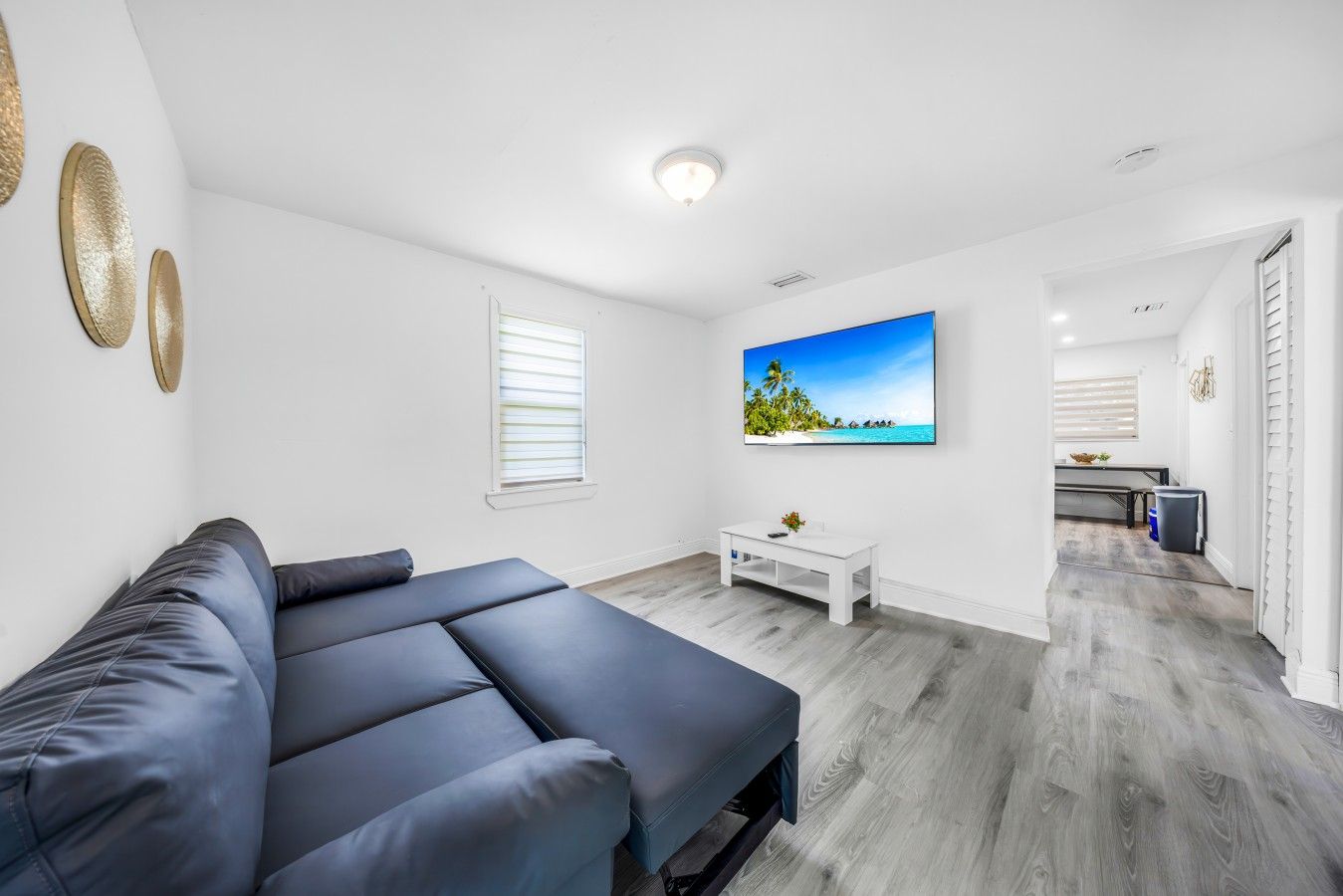 A modern living room with a sectional sofa, a flat-screen TV, and a dining area with a table and chairs.