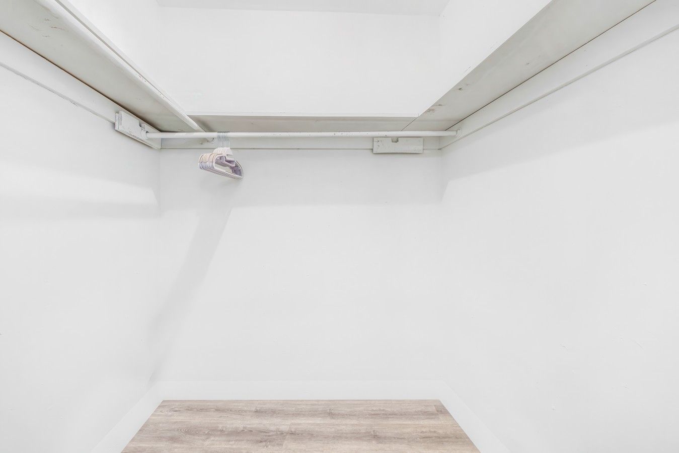 A room with white walls, a wooden floor, and a ceiling vent.