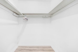 A room with white walls, a wooden floor, and a ceiling vent.